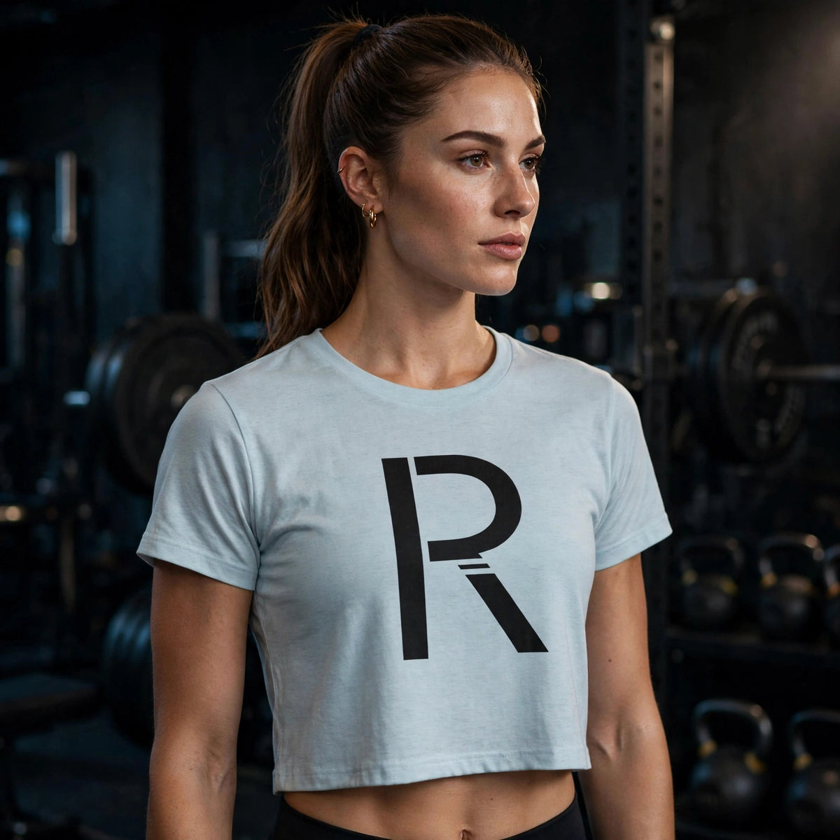 Athletic model in a light blue Ripped City crop tee with large black R, gym setting