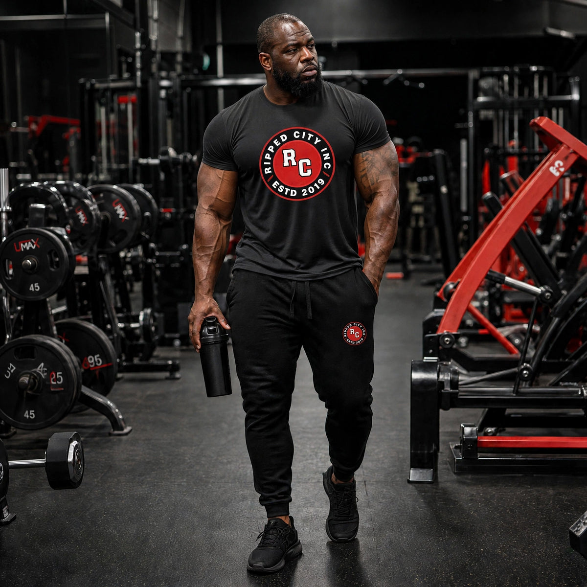 Athletic model in a black Ripped City tee and black joggers with red RC badge, gym scene